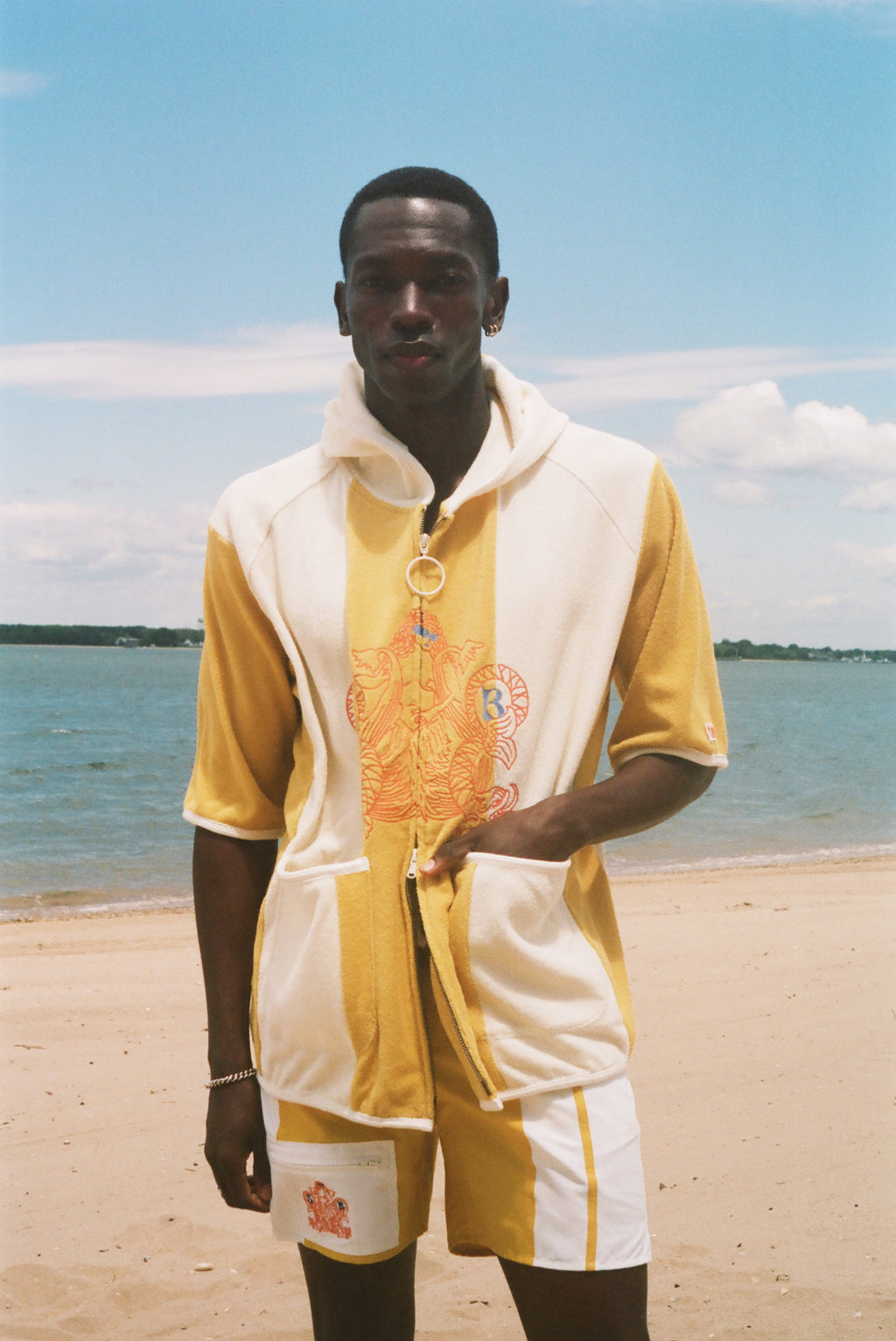 A man standing on a sandy beach wearing a yellow and off-white hooded poncho.