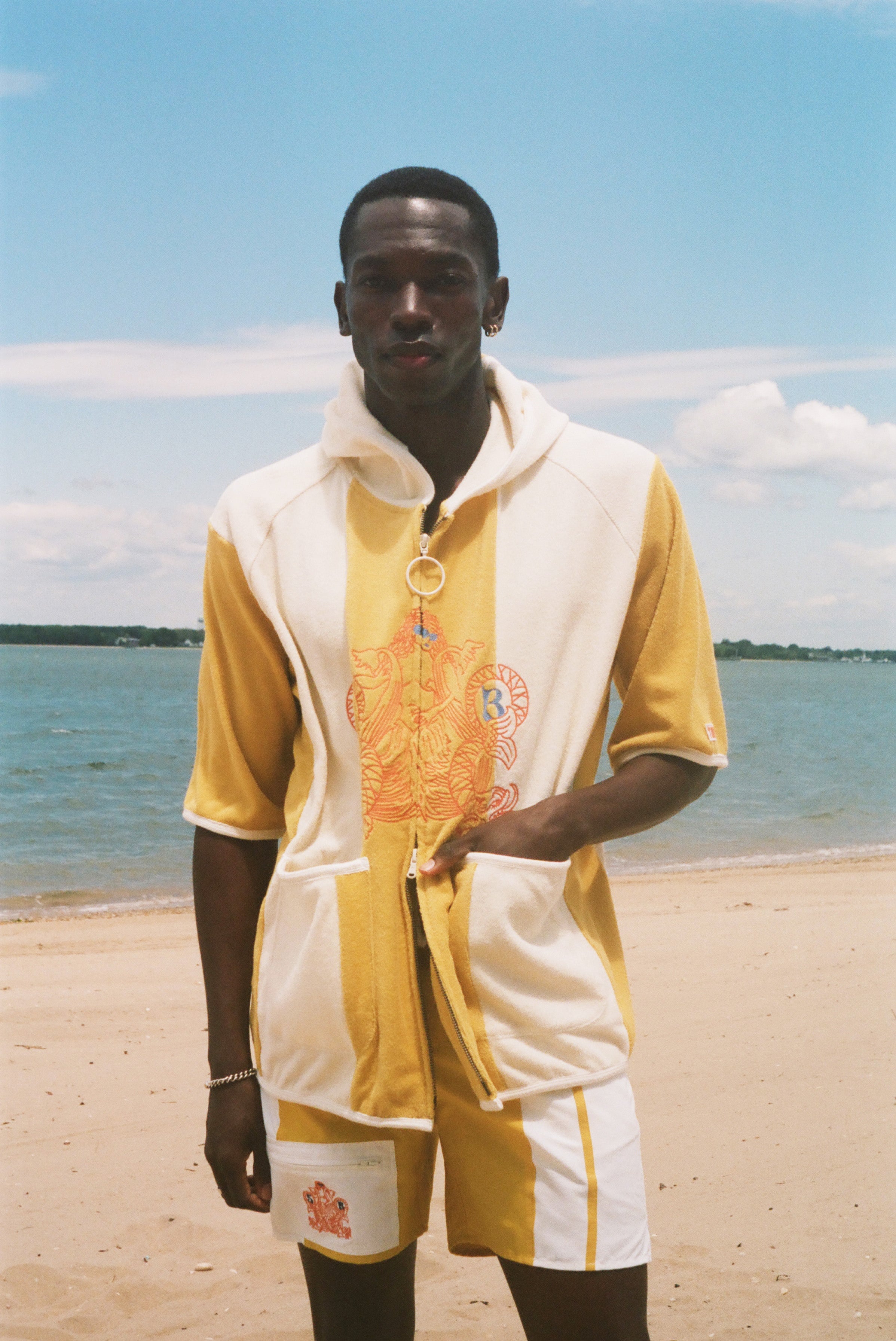 A man standing on a sandy beach wearing a yellow and off-white hooded poncho.