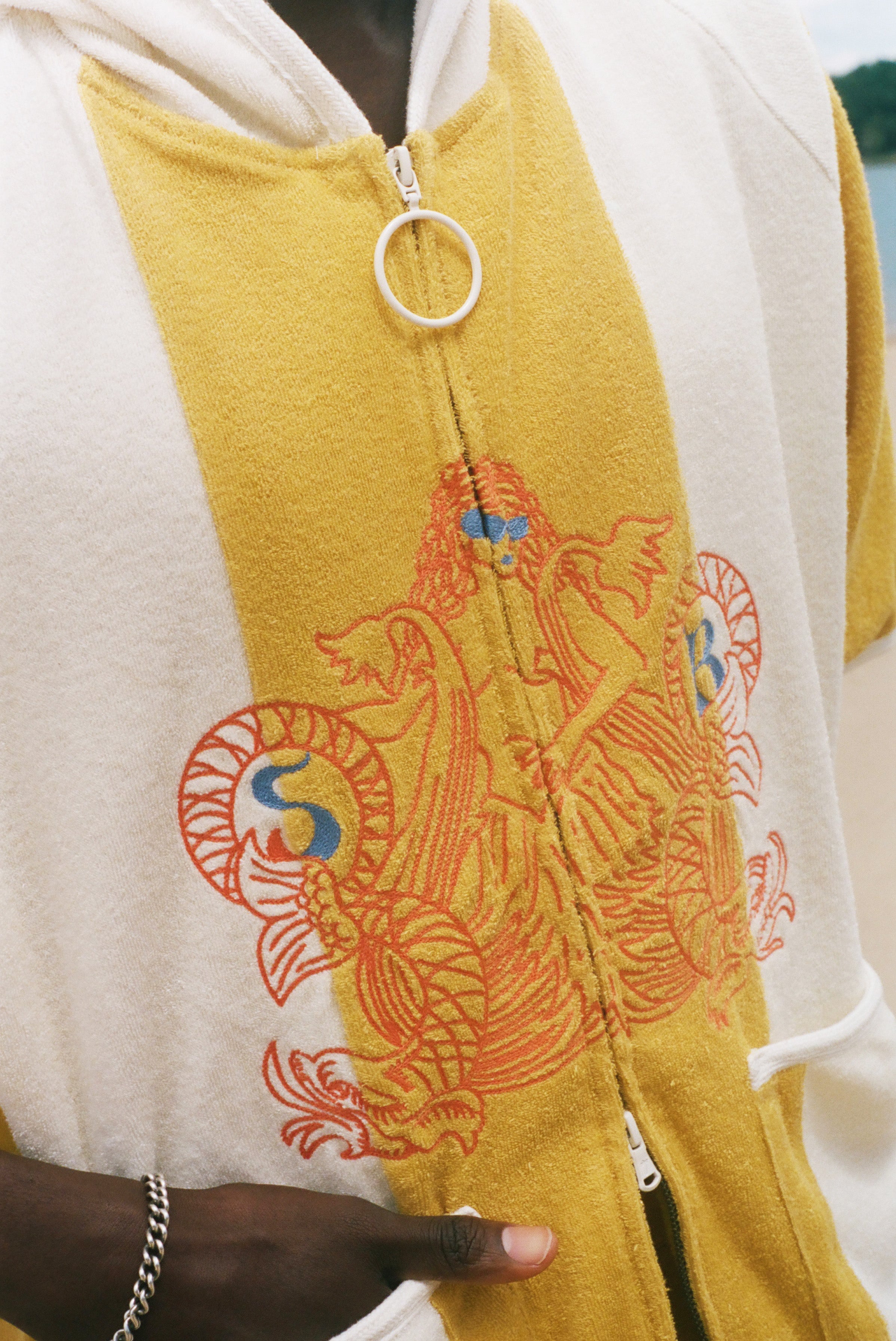 Close-up of a yellow and white zip-up poncho featuring a large orange and blue graphic print on the front, worn by a person.